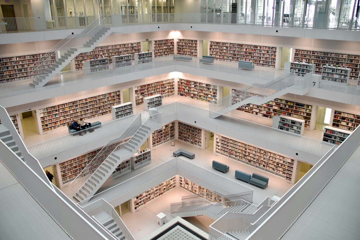 Modern multi-level library interior with white stairs, bookshelves, and seating areas.