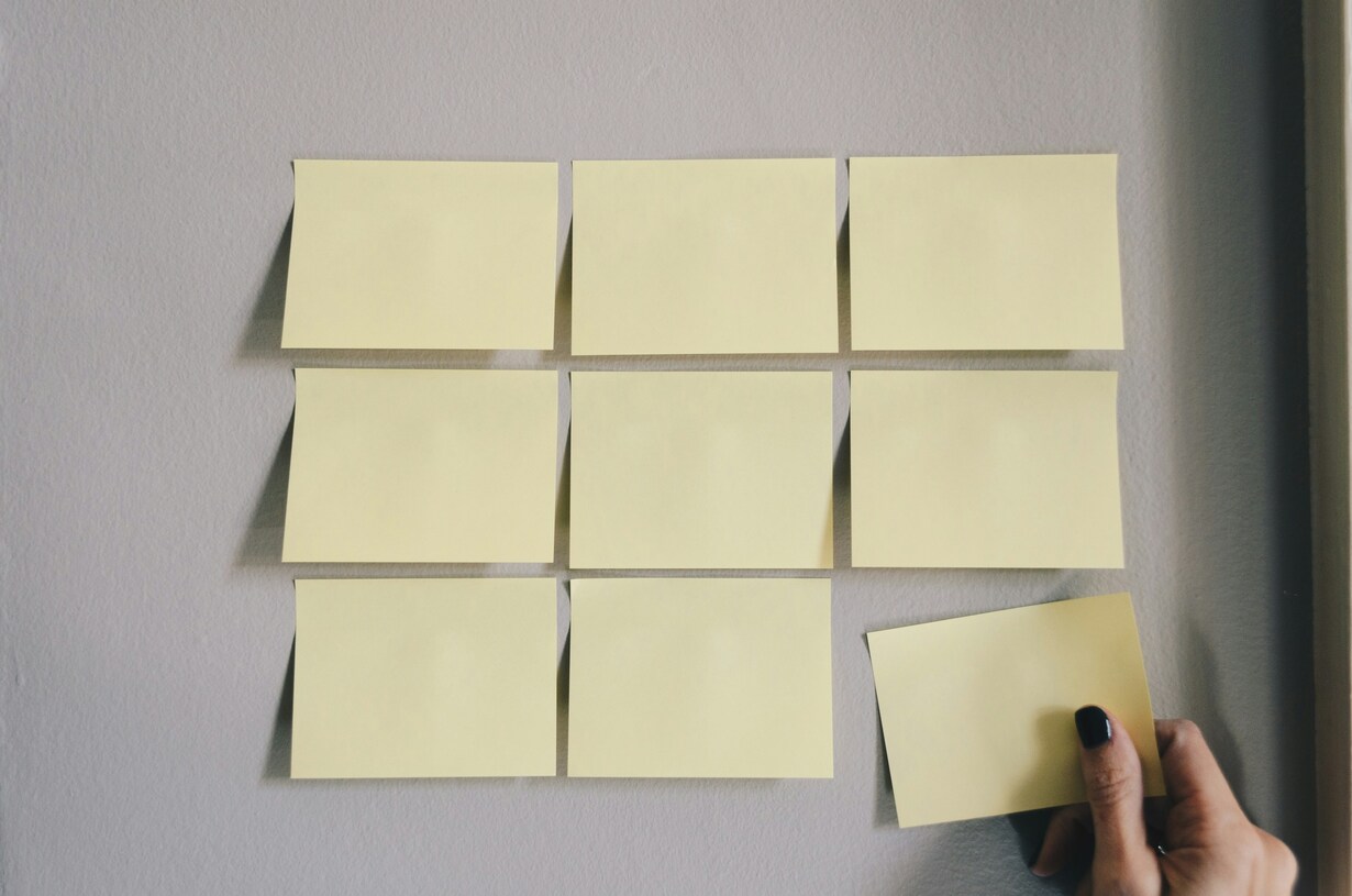 Hand placing a blank sticky note on a wall alongside eight other blank sticky notes.