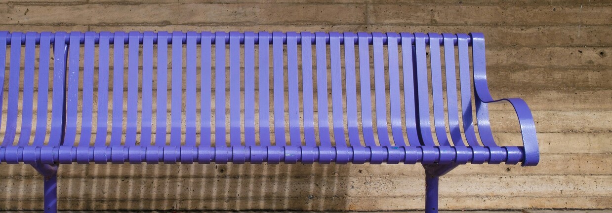 Nahaufnahme von blauer Metallbank vor steinernem Hintergrund.